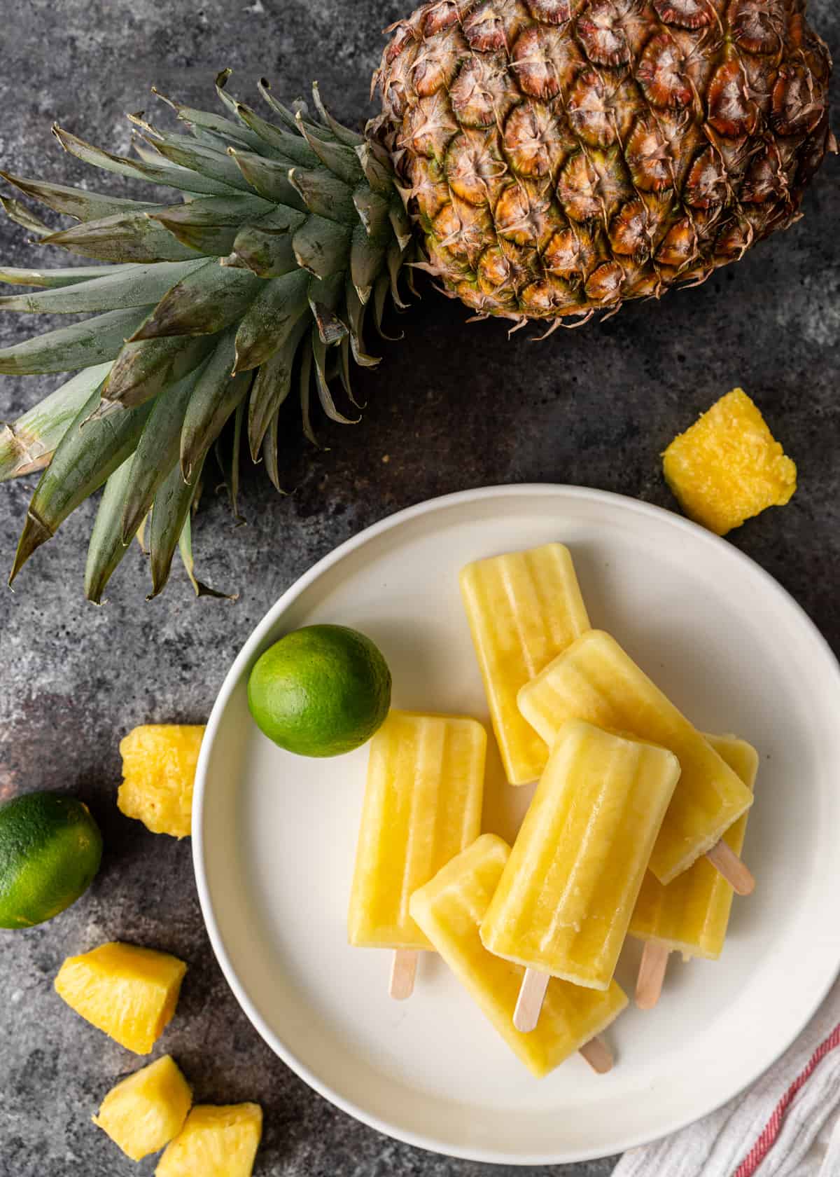 top down view of pineapple ice pops on a white place with limes and pineapple chunks