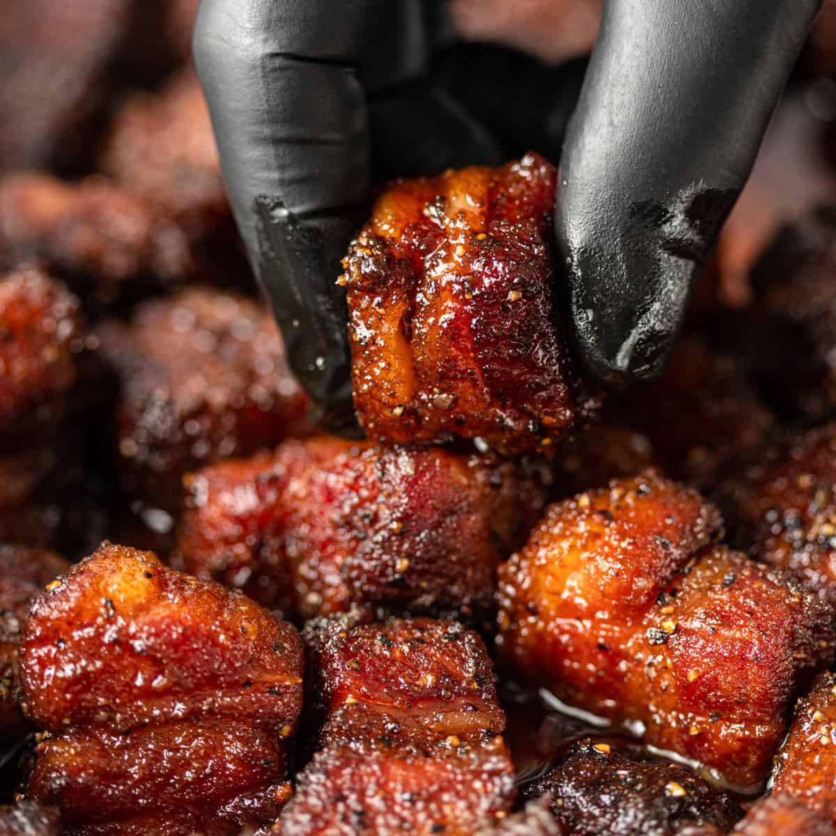 gloved hand holding Pork Belly Burnt Ends