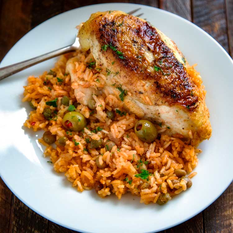 overhead: a white plate of arroz con pollo with olives and fresh herbs