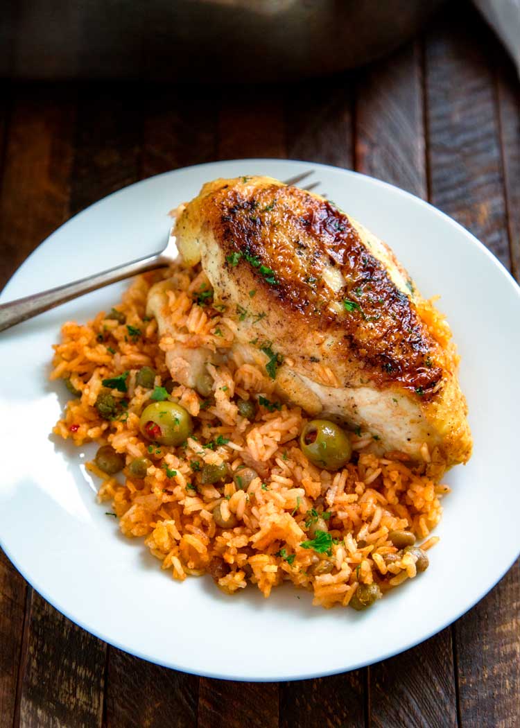 overhead: Puerto Rican chicken and rice on a white plate with olives and herbs