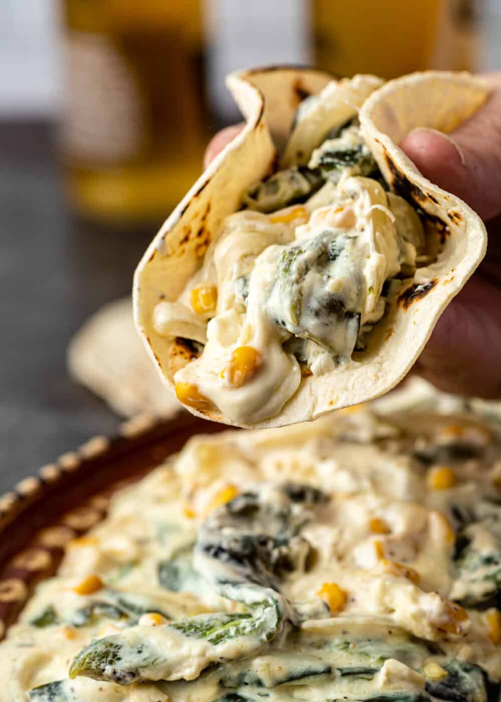 man's hand holding soft taco filled with slices of poblanos in cream sauce