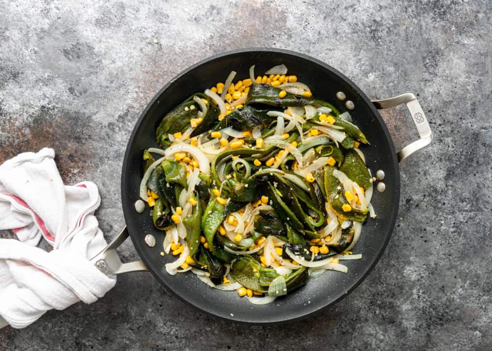 overhead image: corn kernels, white onion slices and strips of poblano peppers sauteing in skillet