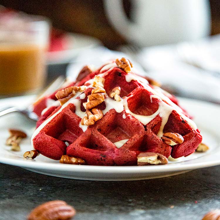 Zoomed in view of Red Velvet Waffles with Cream Cheese Glaze sitting on plate.