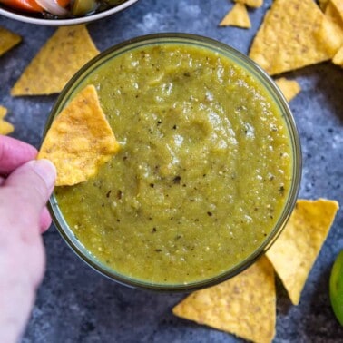 dipping corn tortilla chips into bowl of Mexican tomatillo salsa