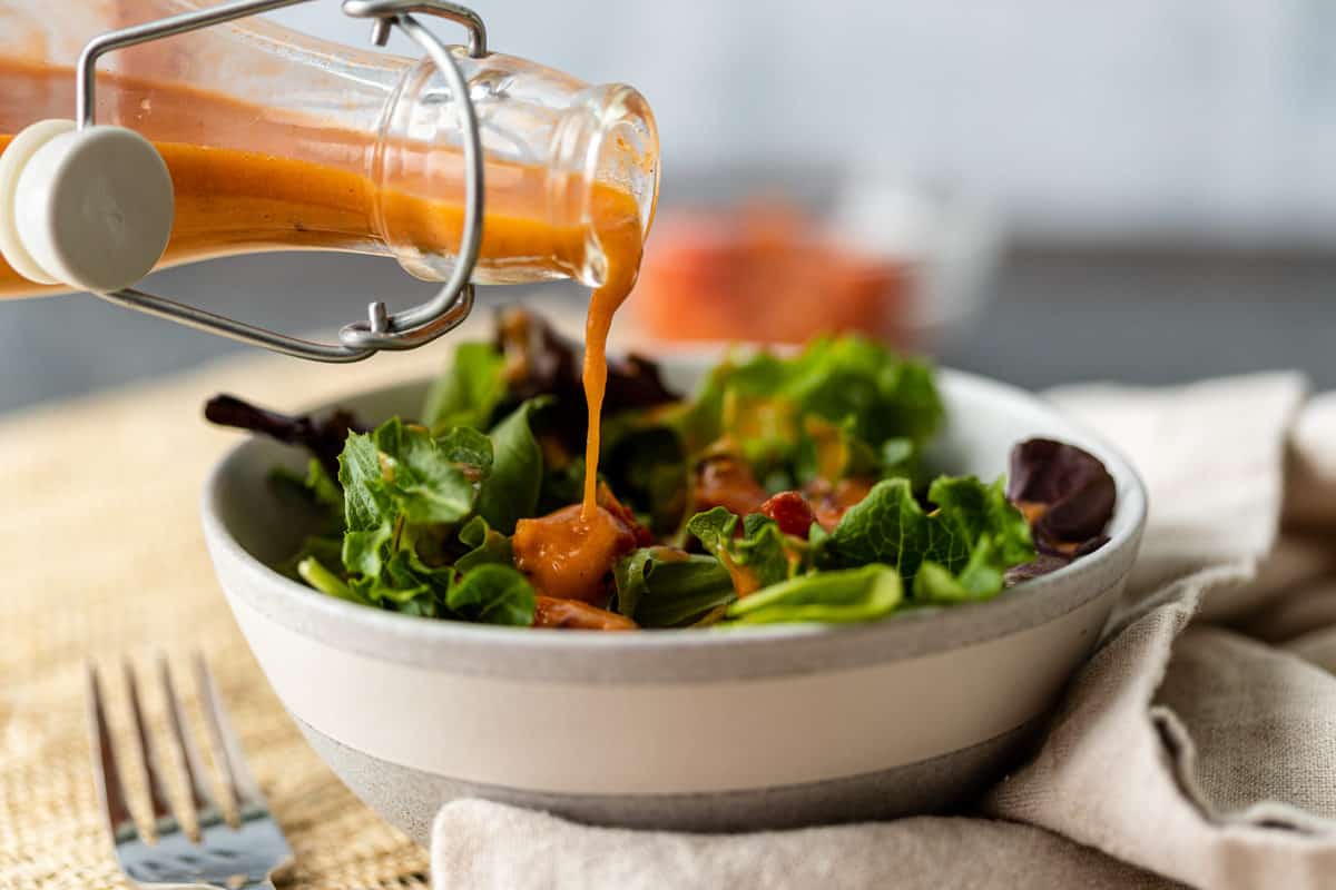 salad in a bowl with Roasted Tomato Vinaigrette being poured on it