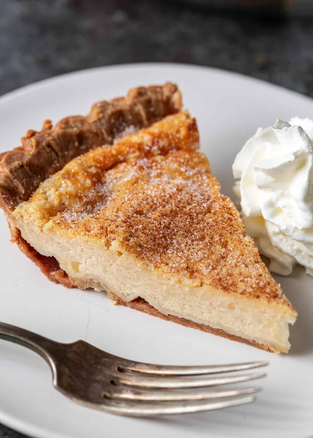 closeup: a slice of buttermilk pie on a plate with a dollop of whipped cream to the side