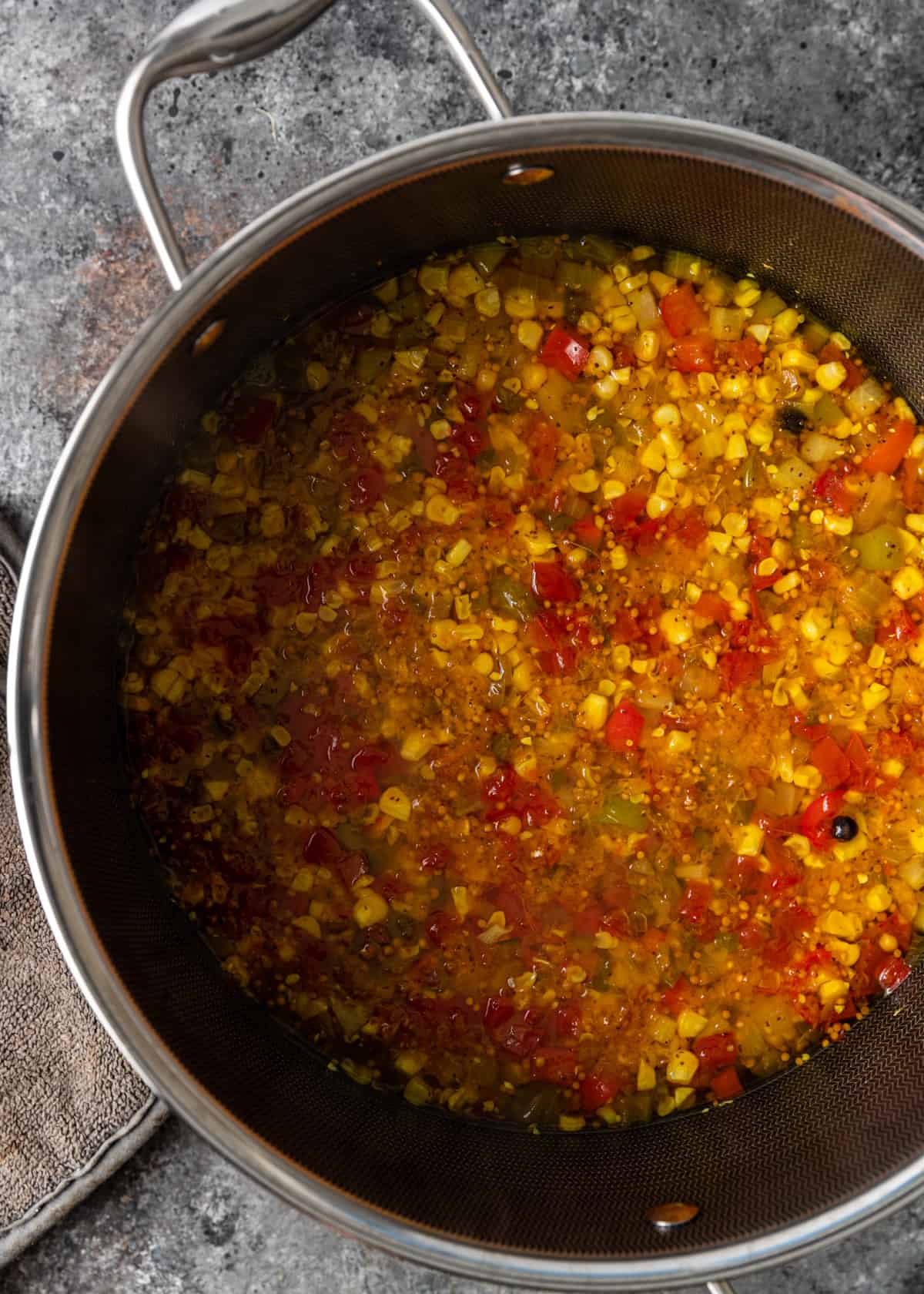 overhead: cooking corn, tomatoes, onion, cucumber, and peppers in a large stock pot