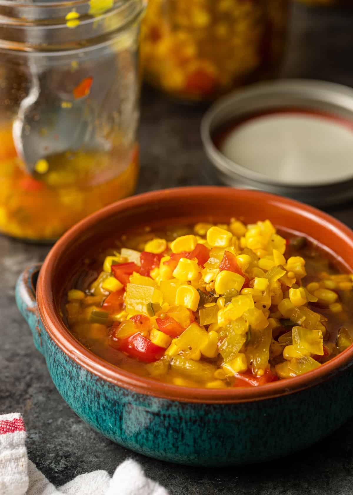 closeup: a ceramic bowl of corn relish with a jar visible in the background