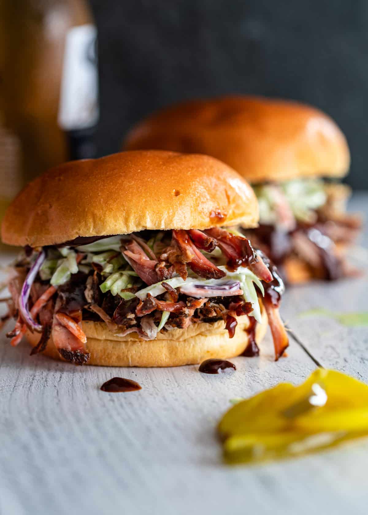 2 pulled pork sandwiches with bbq sauce and coleslaw with pickles with 1 sandwich in focus