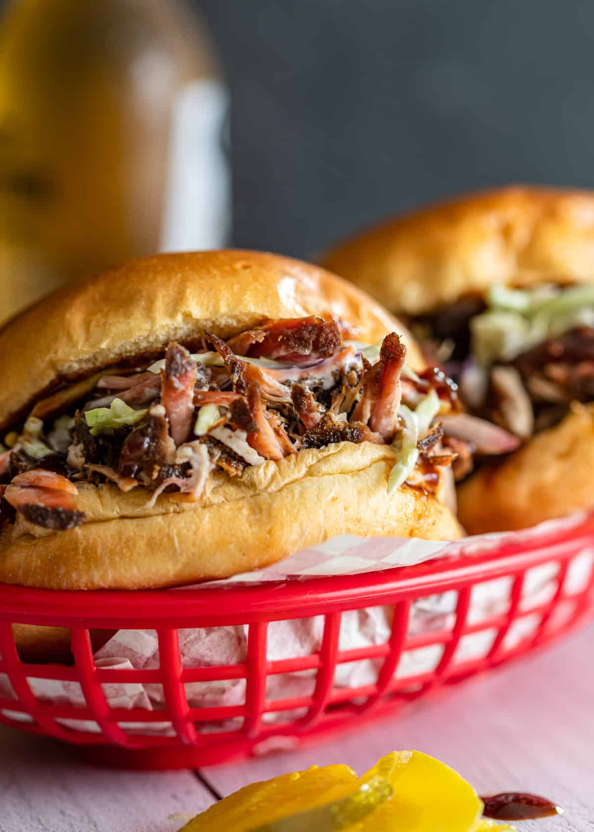 closeup: 2 pulled pork sandwiches with bbq sauce and coleslaw in a red basket with 1 sandwich in focus