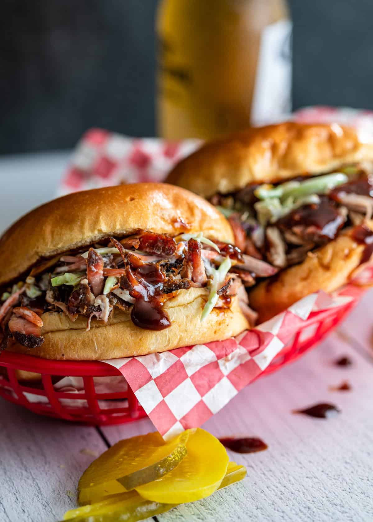 2 pulled pork sandwiches with bbq sauce and coleslaw in a red basket with pickles