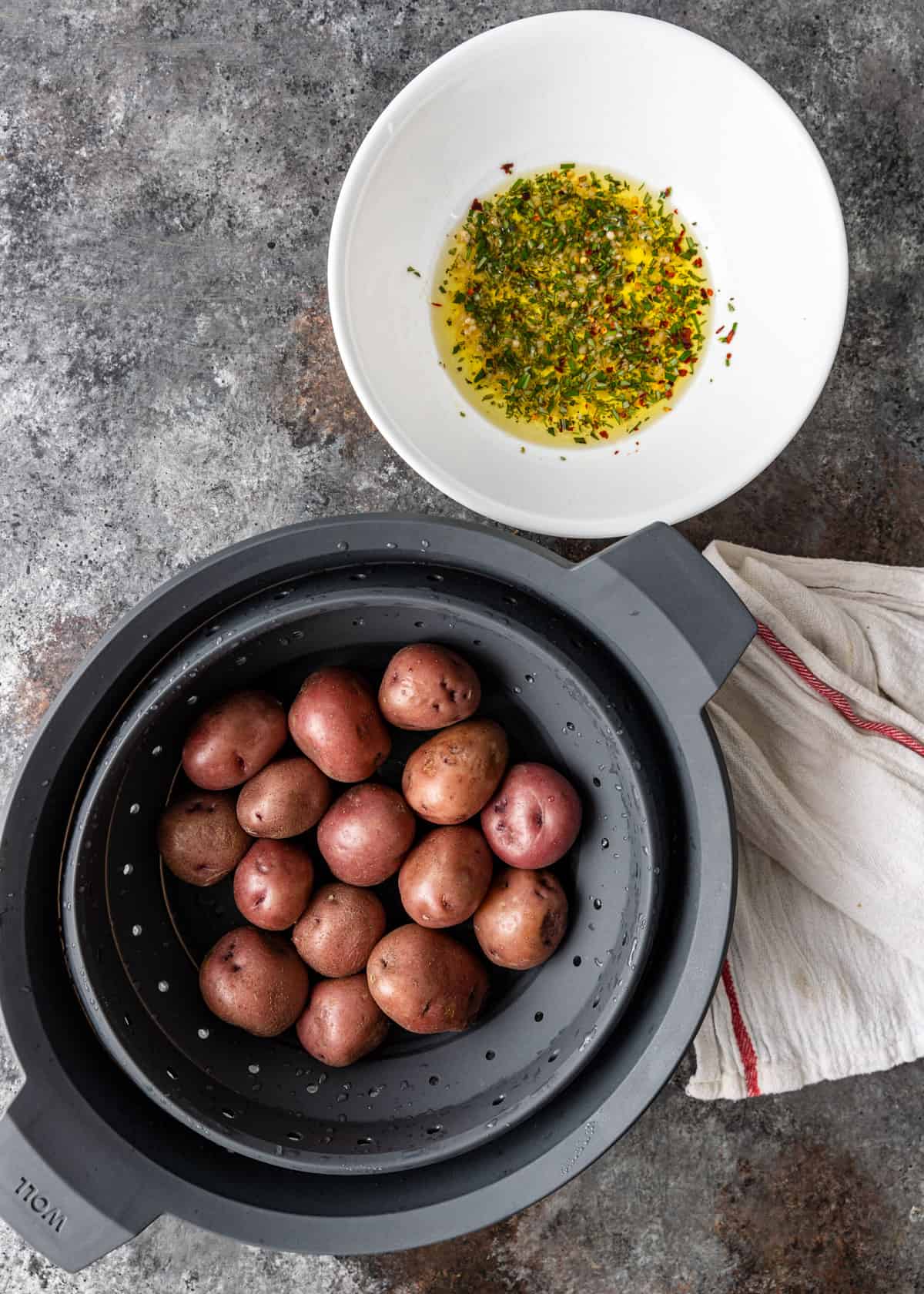 overhead: boiled red potatoes in a colander with herbs and oil in a white bowl