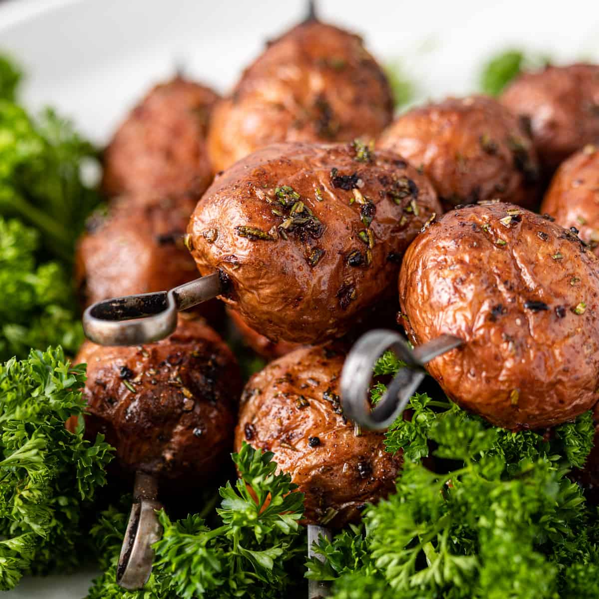 closeup: grilled red potatoes on metal skewers over fresh herbs