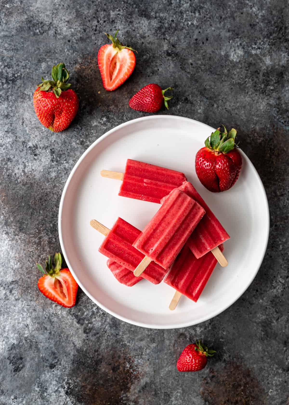 overhead of strawberries and cream ice pops on a white plate with fresh strawberries