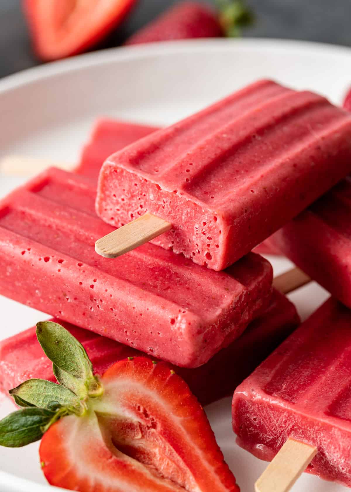 closeup of strawberries and cream ice pops on a white plate with fresh strawberries