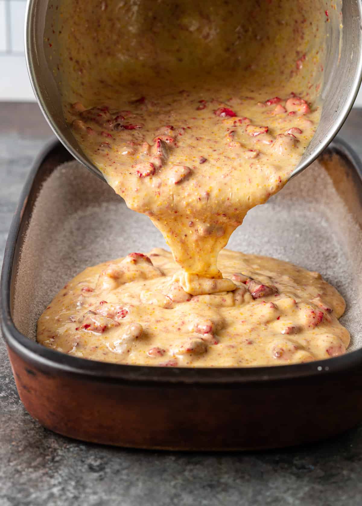 side view: pouring strawberry cornmeal cake batter into a baking dish