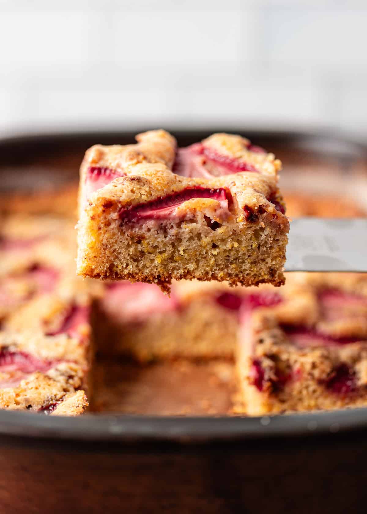 side view closeup: lifting a slice of strawberry cornmeal cake over a baking dish with more cake
