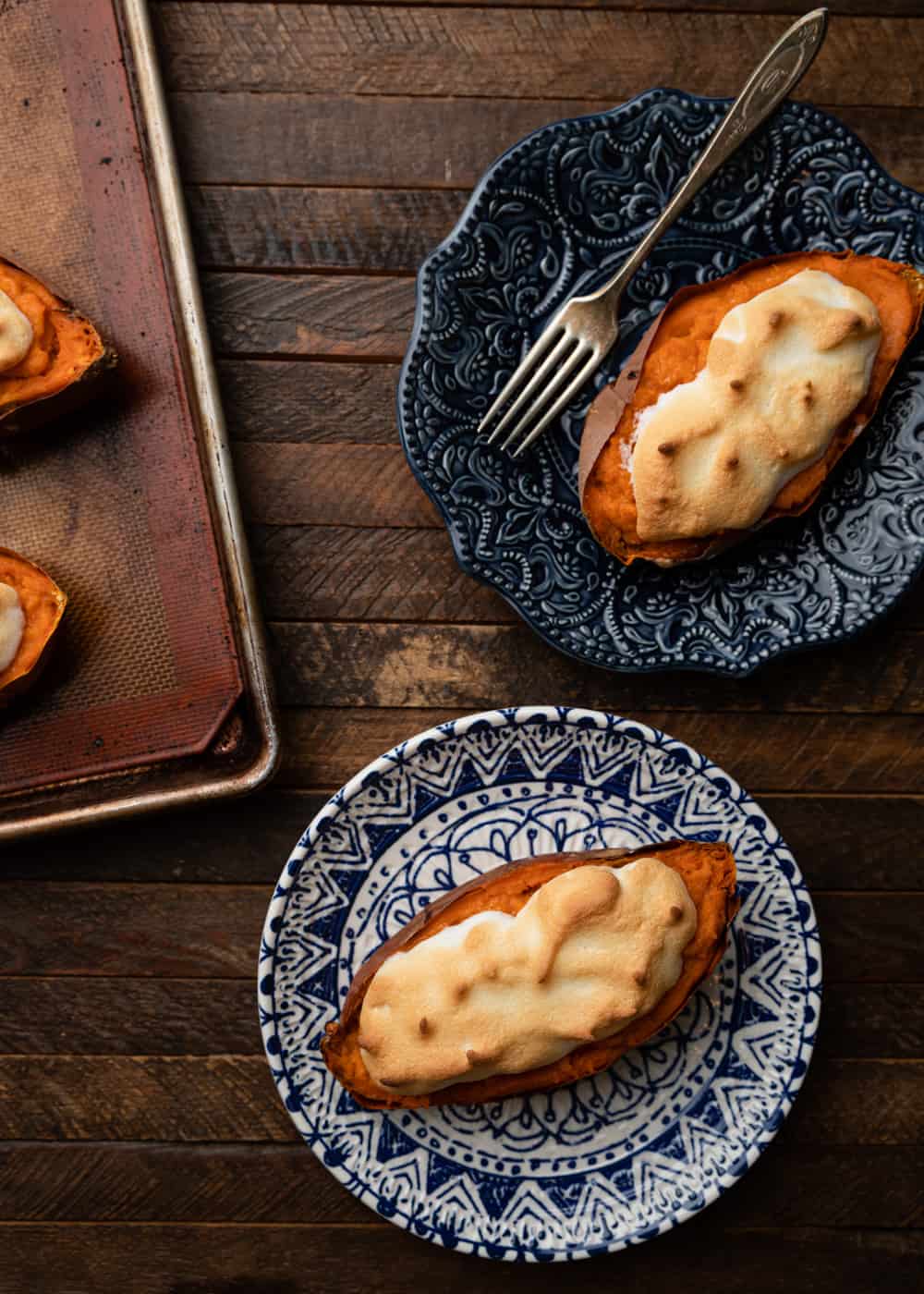 overhead: two blue plates of stuffed sweet potatoes with meringue on top