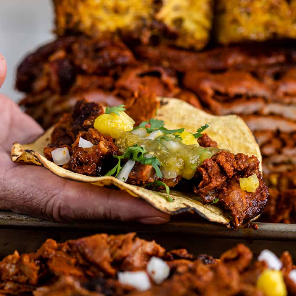 man's hand holding a pork taco al pastor