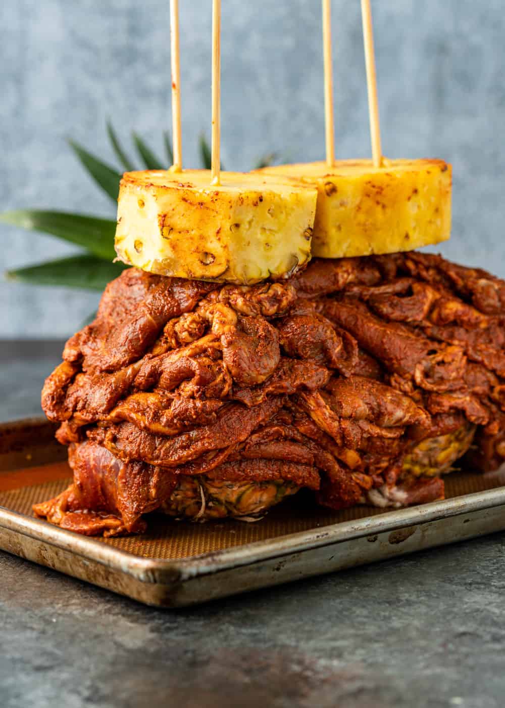 pile of juicy oven roasted Mexican-spiced pork on sheet pan with large pieces of fresh pineapple skewered on top