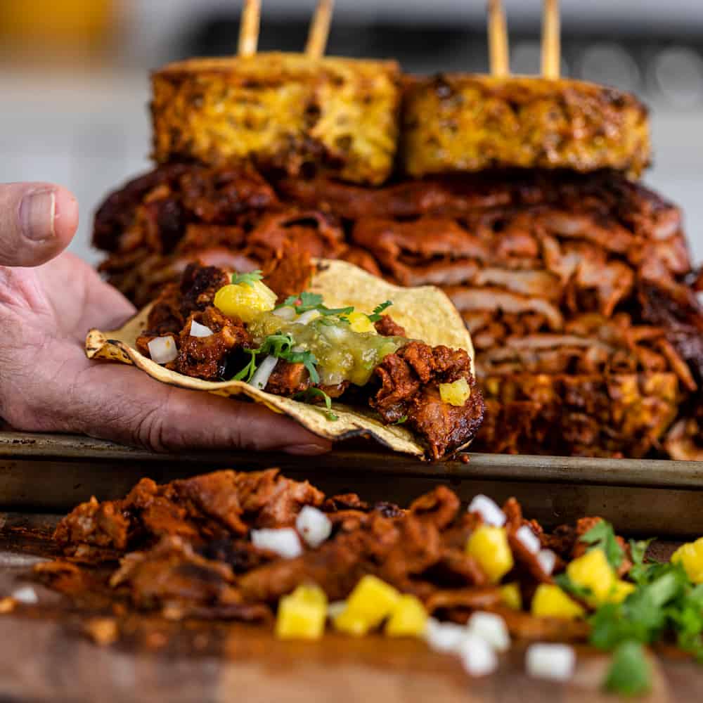 al Pastor taco with grilled, stacked meat behind