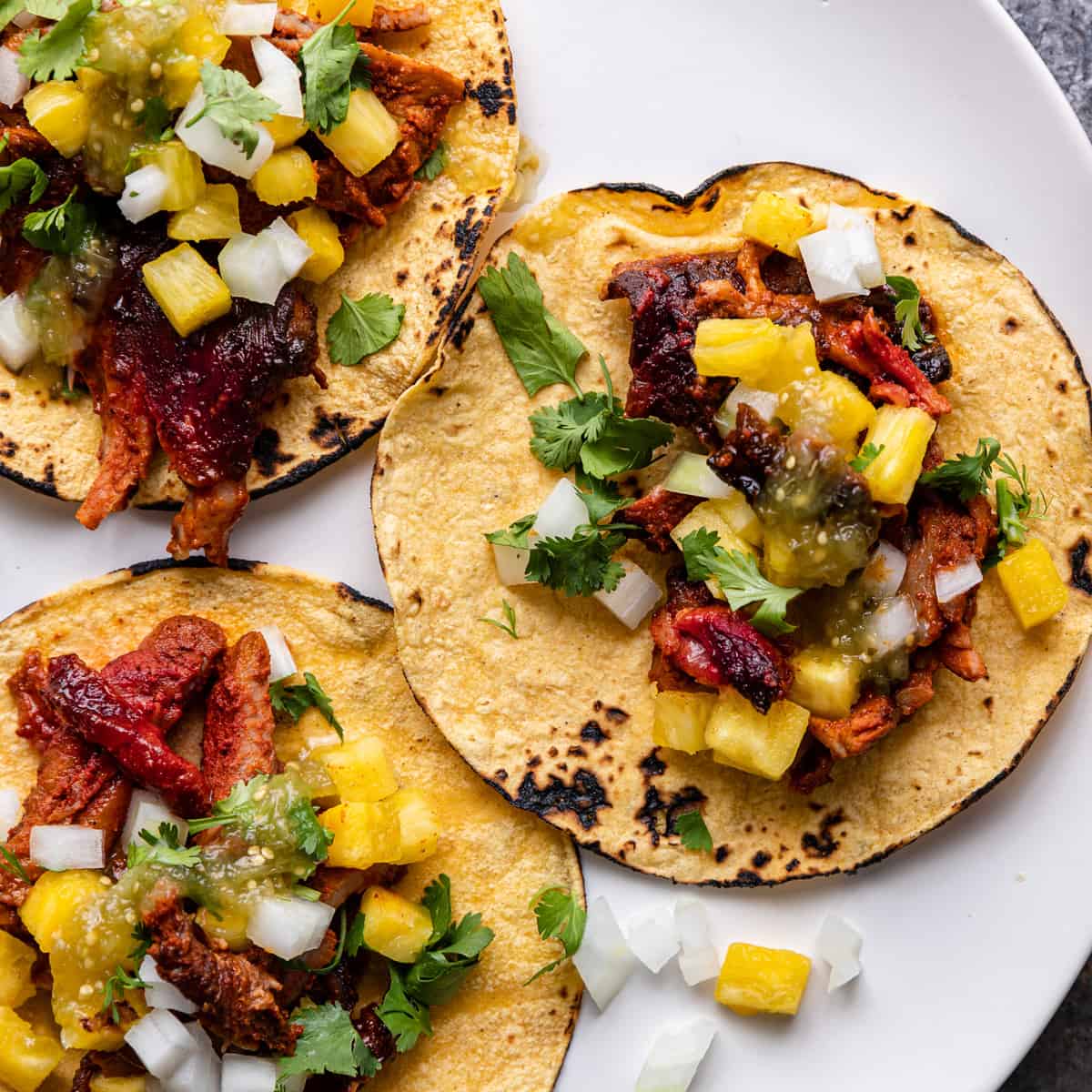 overhead image of 3 tacos al pastor on a white plate