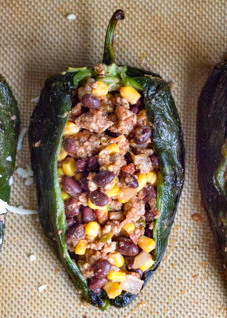 Looking down at a Poblano chile filled with black beans, ground beef, corn and cheese on a baking sheet