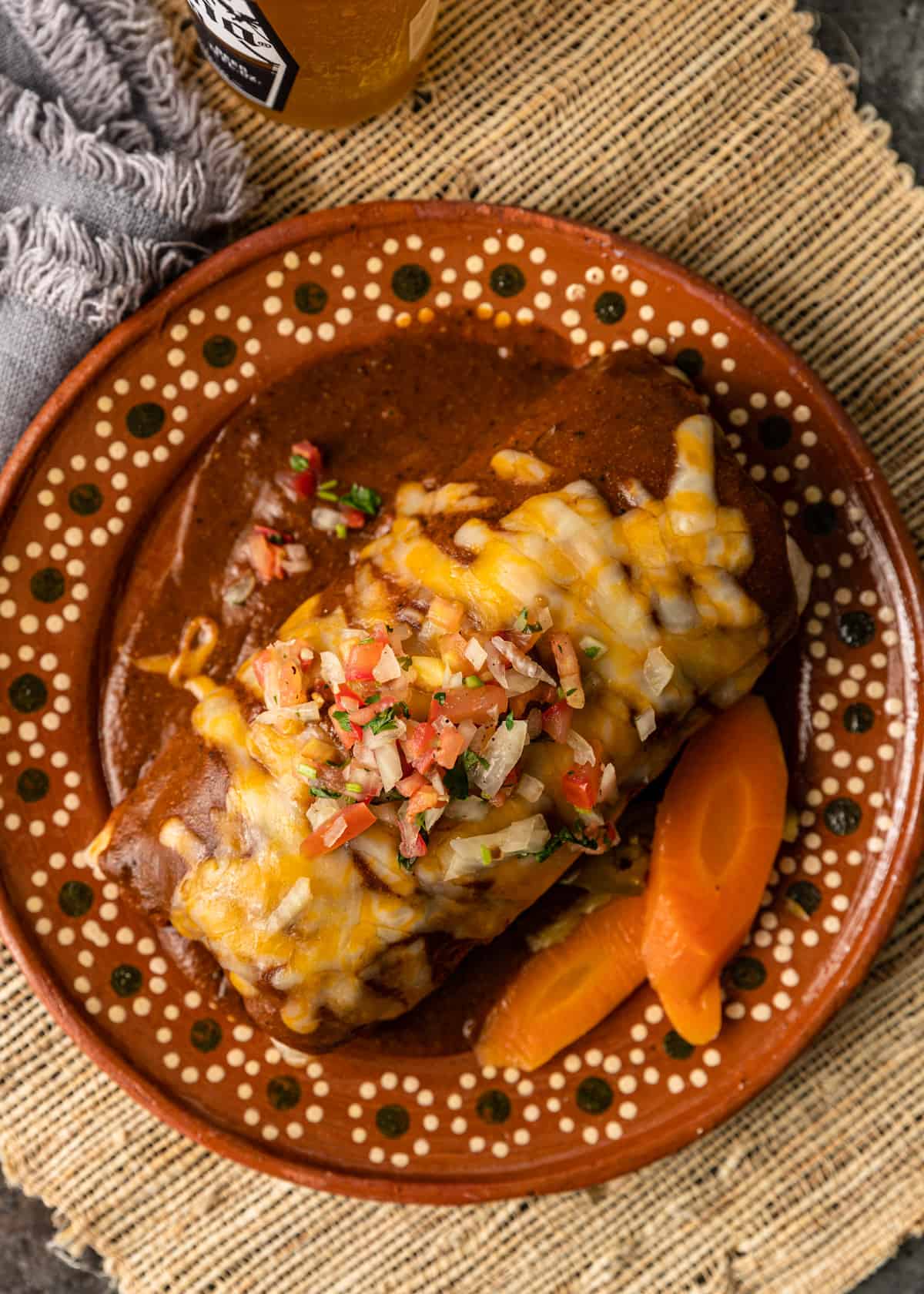 overhead: wet burrito recipe on a ceramic plate with melted cheese and toppings and pickled carrots on the side