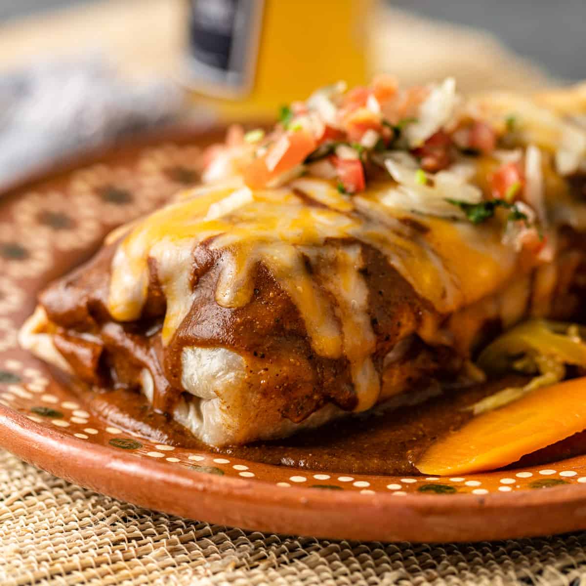 closeup: wet burrito on a ceramic plate with melted cheese and toppings and pickled carrots on the side