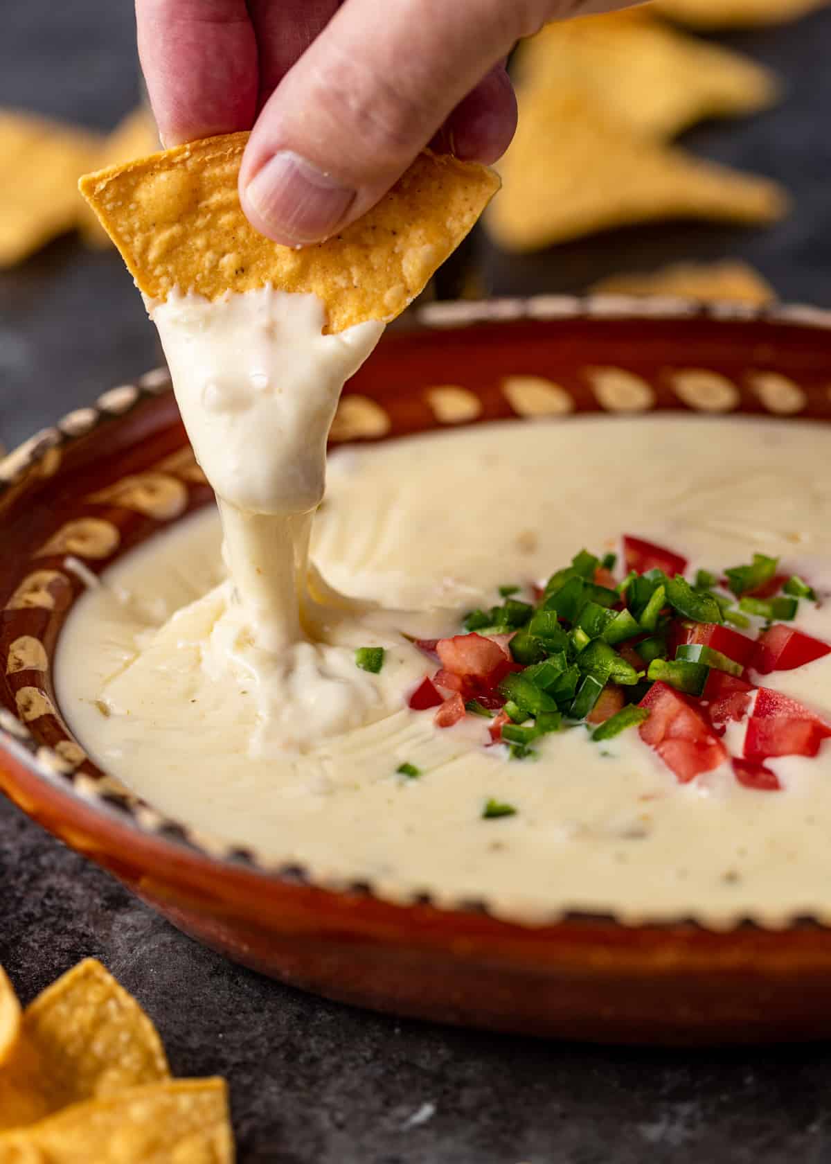 chipotle queso dripping from tortilla chiip into bowl of chile con queso