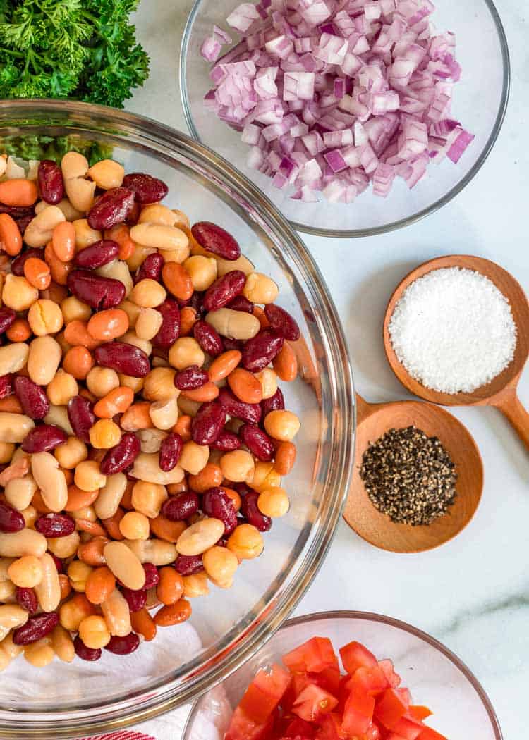 large bowl of mixed beans next to small bowls of diced red onion, salt, and black pepper